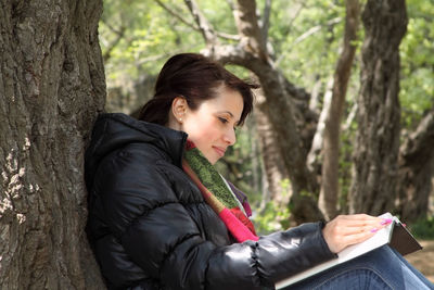 Side view of young woman sitting on tree trunk