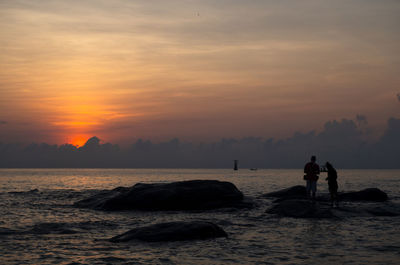 Silhouette people on beach against sky during sunset