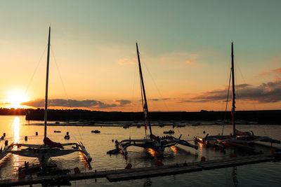 Sailboats moored on sea against sky during sunset