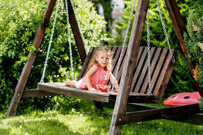 A little girl is lying on a garden swing and eating fresh strawberries