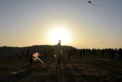 People playing soccer on field against sky during sunset