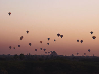 Hot air balloons flying over silhouette landscape against sky during sunset