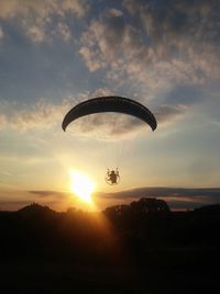 Silhouette person powered paragliding against sky during sunset