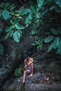 Shirtless man sitting on rock