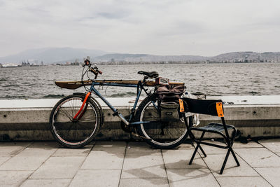 Bicycle parked by sea against sky