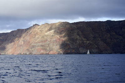 Scenic view of sea by mountain against sky