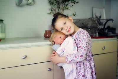 Cute european kid girl with baby doll in sling. motherhood and role-playing, child development