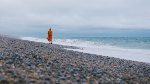 Rear view of monk on beach against sky