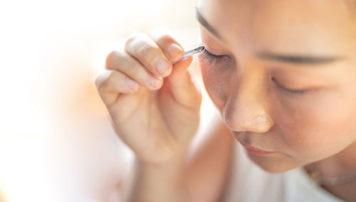 Female hand holding the eyelash and preparing to attach it to her eye.