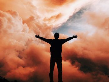 Silhouette man standing with arms outstretched against sky during sunset