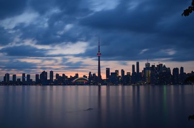 Sea against cn tower amidst buildings in city at sunset