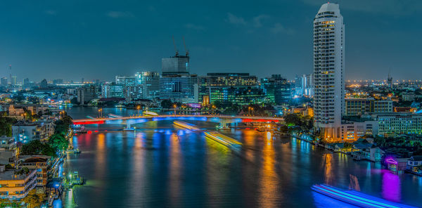 Illuminated buildings by river against sky in city