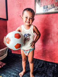 Full length portrait of boy holding soccer ball at home