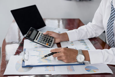 Midsection of businessman using calculator on table