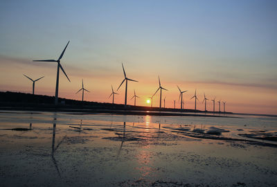 Wind turbines on land against sky during sunset