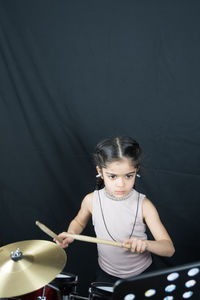 Cute girl playing drum set against black backdrop