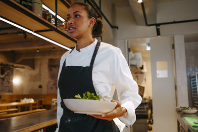 Female chef walking with salad bowl at commercial kitchen