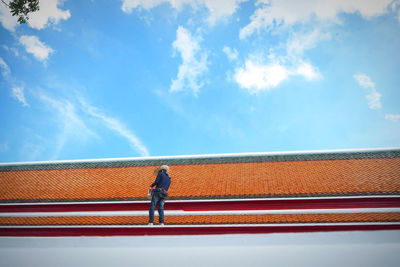 Low angle view of man standing on railing against blue sky
