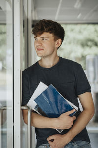 Thoughtful male holding books leaning on door in university