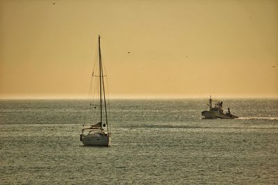 Sailboat sailing in sea against clear sky during sunset