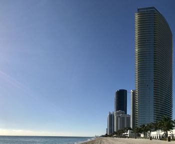 Sea by modern buildings against clear blue sky