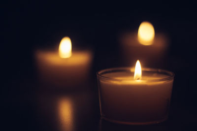Close-up of tea light candles burning in darkroom