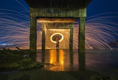 Man spinning wire wool under pier in sea at night
