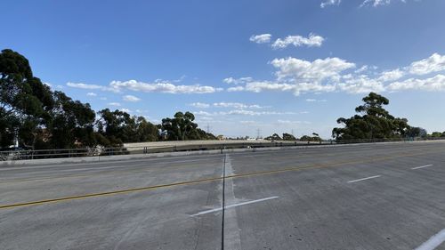 Empty road by trees against sky