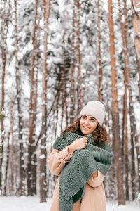 A smiling girl with a green scarf stands in a snowy forest in winter and looks away