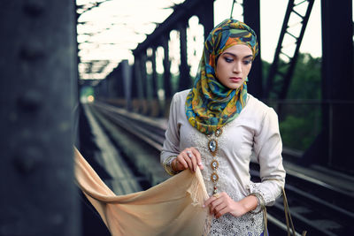 Young woman wearing hijab looking down while standing at railway bridge