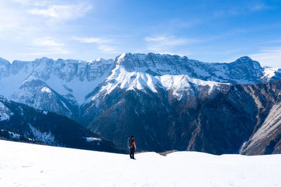 Rear view of man walking on snowcapped mountains against sky