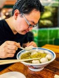 Close-up of young asian man eating noodles and fish balls in soup.