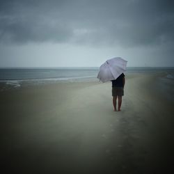 Rear view of woman standing at beach against sky