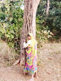 Full length of woman standing by tree trunk