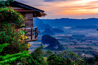 House by trees and mountains against sky during sunset