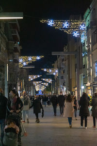 People walking on illuminated street amidst buildings at night