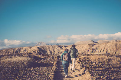 Rear view of man walking on mountain against sky