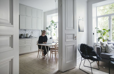 Businesswoman using laptop on table seen through doorway at home