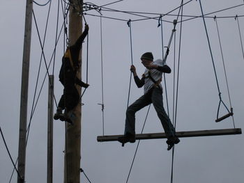 Low angle view of man hanging on rope against sky