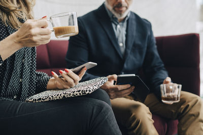 Midsection of business people using mobile phones and having tea on couch during conference