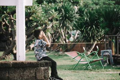 Girl sitting on seat against trees