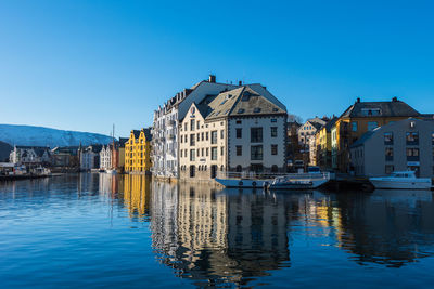 Sailboats in canal amidst buildings against blue sky