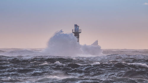 Lighthouse by sea against sky during sunset