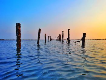 Wooden posts in sea against sky during sunset