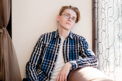 Portrait of young woman sitting against wall at home