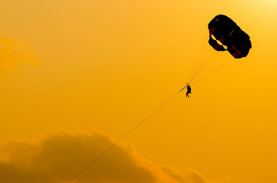 Low angle view of silhouette person paragliding against sky during sunset