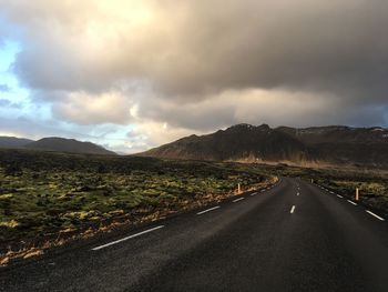 Road passing through landscape against storm clouds
