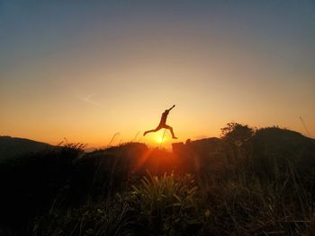 Rear view of man standing on field against sky during sunset