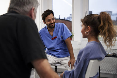 Male doctor talking to girl patient and grandfather during appointment