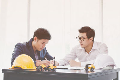 Male architects drawing blueprint at desk in office